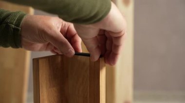 Adamın biri bir parça yumuşak bandı bir mobilyanın tahta bacaklarına yapıştırıyor. Bir adam mobilya montajı yapıyor..