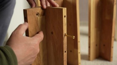 Bir adam ahşap bir mobilya parçası tutuyor ve ona vida takıyor. Ahşap mobilyalar monte ediliyor.