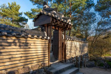 Tahta kapılı taş bir duvar. Kapı açık.