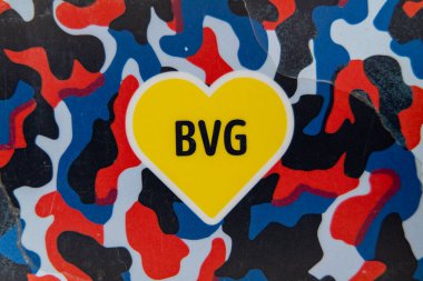 Almanya 7 Nisan 2025. Berlin 'deki toplu taşıma logosu. Üzerinde BVG harfleri olan sarı kalp. Kalp mavi, kırmızı ve siyah arkaplanda