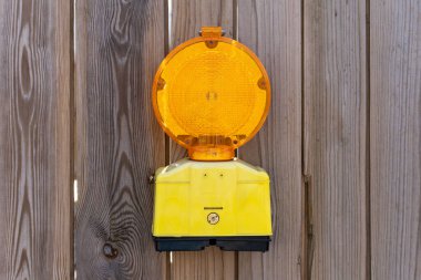 Ahşap bir çite asılı sarı ve siyah bir trafik ışığı var. Işık yanıyor ve yanıyor.