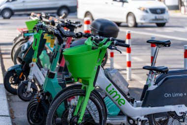 Almanya 10 Nisan 2025. Yolun kenarına bir sıra kireç mobilet park edilmiş. Arka planda birkaç bisiklet daha var.