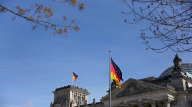 Reichstag binasının üstünde iki bayrak dalgalanıyor. Mavi gökyüzünde Alman bayrakları.