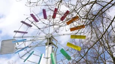 Renkli bıçaklı bir yel değirmeni direğin üstündedir. Bıçaklar farklı renklerde ve daire şeklinde dizilmiş.