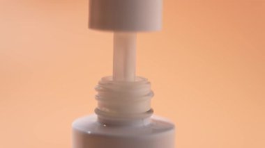 Beyaz kozmetik ürünü ve turuncu arka planda pipeti olan beyaz bir şişe. Beyaz kozmetik sıvısı pipetten şişeye damlıyor..