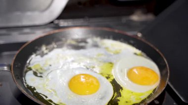 Tavada iki yumurta pişiyor. Biri sarı ve diğeri beyaz. Tava ocağın üstünde.