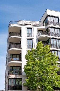 Balkonları olan yeni modern bir bina. Yanında yeşil ağaç büyüyen yeni bina.
