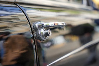 Klasik siyah arabanın krom kapı kolunun arka görüntüsü. Arka krom kapı kolunun perspektif görüntüsü. Siyah arabanın silindirik kilidi var. Yansıtıcı boya sokak görüntülerini yakalıyor..