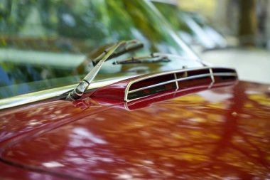 Kırmızı bir vintage arabanın yakın çekimi. Ağaçların altındaki hava girişli ve parlak boyalı araba..