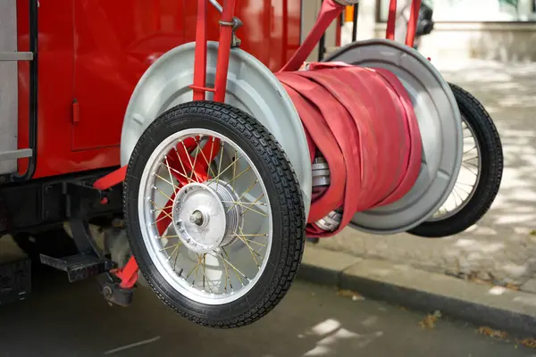 Klasik itfaiye ekipmanı. Tekerlekli hortum makarası ve sarmalanmış kırmızı yangın hortumu acil durum hizmetlerinde kullanılmak üzere hazır..