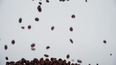 Düşen kahve çekirdekleri beyaz arka plandaki ekranı doldurur. Düşen kahve çekirdekleri yavaş çekimde ekranı dolduruyor..