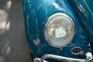 Almanya 11 Mayıs 2025. Mavi bir Beetle 'ın ön farları. Mavi bir Volkswagen Beetle 'ın ön farının yakın çekimi. Görünür ağaç yansımaları olan yansıtıcı yüzey.