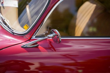 Almanya 11 Mayıs 2025. Klasik bir Ca 'nın yan aynasına ve kapısına yakın çekim. Krom kaplama bir yan aynanın ve kırmızı klasik bir arabanın kapısının yakın çekimi. Parlak yüzey çevreyi yansıtır ve zamansız zarafeti taşır..