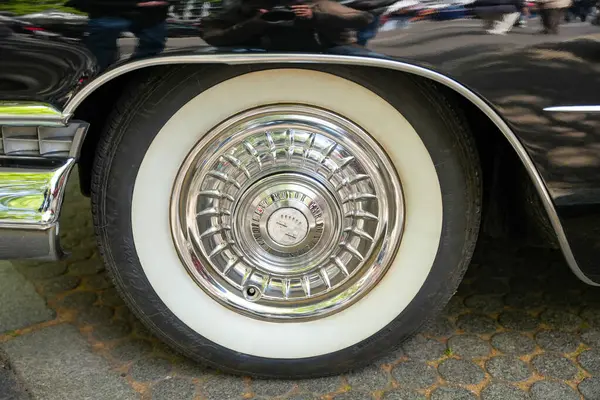 Almanya 11 Mayıs 2025. Cadillac jant kapaklı Whitewall lastiği. Tipik bir Cadillac jant kapağı olan parlak beyaz duvar lastiği 1950 'lerin Amerikan lüksünü temsil ediyor. Yansıma klasik bir araba kongresi sahnesini gösteriyor..