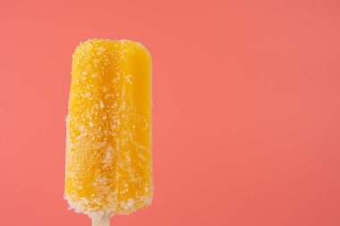 Pembe arka planda buz kristalleri olan tek bir donmuş mango dondurması. Zıt renkler modern, taze bir yaz havası yaratır..