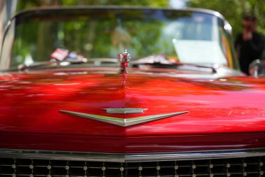 Almanya 11 Mayıs 2025. Üzerinde amblem olan üstü açık bir arabanın ön görüntüsü. Kaputunda klasik bir amblem olan üstü açık parlak kırmızı bir Cadillac. Parlak yüzey gökyüzünü ve etrafındaki ağaçları yansıtıyor..