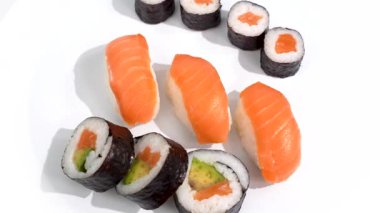 Suşi beyaz arka planda dönüyor. Beyaz tabakta renkli somon ve avokado suşisi seçimi. Bileşimi farklı renklerle temiz ve şık..