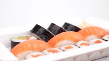 Dönen suşi kutusunun yakın görüntüsü. Çeşitli suşi dürümleri ve nigiriler iştah açıcı bir şekilde beyaz bir kutuda sunuluyor. Yan taraftan çekiliyor ve küçük detayları gösteriyor..