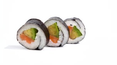 Arka arkaya üç maki suşi, beyaz arka planda döner. Üç somon ve avokado suşi rulosu birbiri ardına konur. Malzemelerin katmanı açıkça görülüyor..