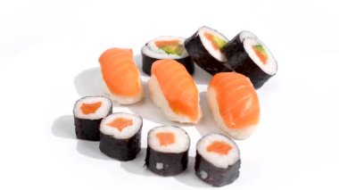 Suşi seçimi beyaz arkaplanda dönüyor. Beyaz bir tabakta bir sıra nigiri ve maki suşi servis edilir. Somon ve avokado kombinasyonu uyumlu bir renk şeması yaratır..