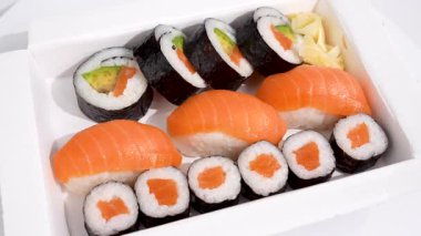 Somon ve avokado suşi kutusu beyaz arka planda döner. Taze somon ve avokado suşisi iştah açıcı bir şekilde beyaz bir kutuda sunulur. Nigiri ve maki 'nin kombinasyonu renk ve tazeliği ile etkiler..