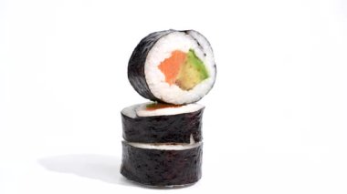 Beyaz arka planda dönen üç suşi rulosu. Üç suşi rulosu zarif bir şekilde istiflenmiş, üsttekinde bir dilim somon ve avokado var. Hafif bir sırt deliğinde şık bir kompozisyon