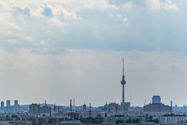 Uzakta, Berlin TV Kulesi bulutlu gökyüzüne yükseliyor. Ufuk çizgisi, başkentin tipik bir şehir manzarası olan detaylı ve geniş bir şekilde zengin görünüyor..