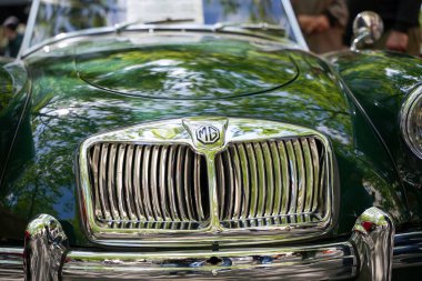 Almanya 11 Mayıs 2025. MG Vintage Car Front Green. Parlak krom ızgaralı ve koyu yeşil boyalı klasik bir MG vintage araba. Ağaçların yansıması zarif, nostaljik izlenimi arttırır..