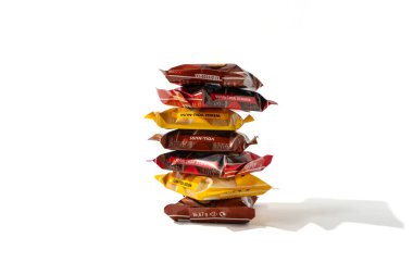 Bir yığın renkli mini Ritter spor barı gevşek bir şekilde üst üste yığılmış. Farklı isimlere sahip barlar dağınık bir şekilde istiflenmiş. Beyaz arkaplanda izole edilmiş çikolata çubukları.