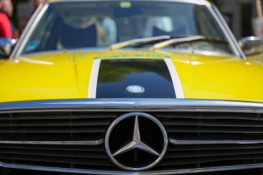 Almanya 11 Mayıs 2025. Bu yakın plan, siyah çizgili ve ikonik yıldız logosu olan sarı bir Mercedes 'in önünü gösteriyor. Araba son derece parlaktır ve kaputun etrafını yansıtır..
