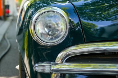 Almanya 11 Mayıs 2025. Klasik krom çerçeveli klasik bir Ford 'un yuvarlak farının ayrıntıları. Arabanın parlak boyası ağaçları yansıtıyor ve nostaljik bir atmosfer yaratıyor..