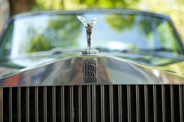 Kaputu ve logosu olan bir Rolls-Royce 'un ön görüntüsü. Klasik bir amblem ve parlak kaput süsüsüyle muhteşem bir Rolls-Royce görüntünün merkezine hükmediyor. Araba, İngiliz otomotiv geleneğini ve lüksünü simgeliyor..