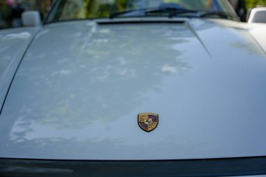 Kaputta Porsche logosu var. Geleneksel Porsche arması beyaz bir klasiğin kaputunu süslüyor. Marka sembolizmine odaklanmış minimalist bir çekim..