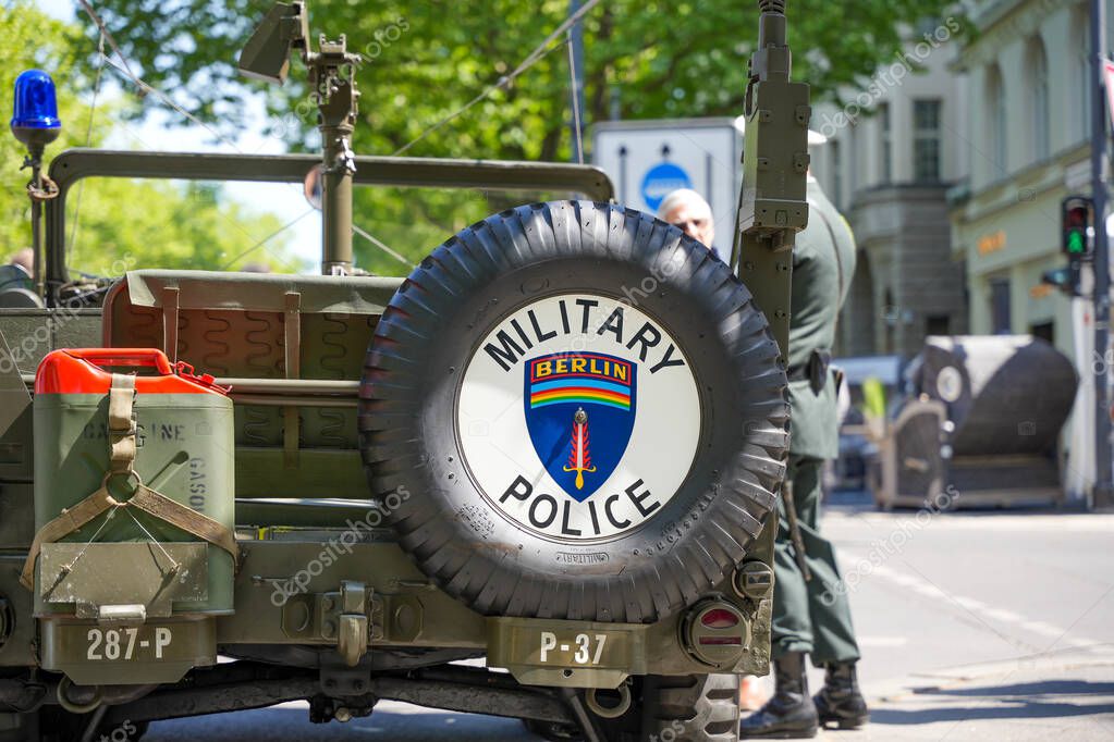 Germany Berlin May 11, 2025. A historic military vehicle with a spare tire bearing the emblem of the Military Police Berlin. In the background, you can see soldiers in uniform and a street scene with passersby.