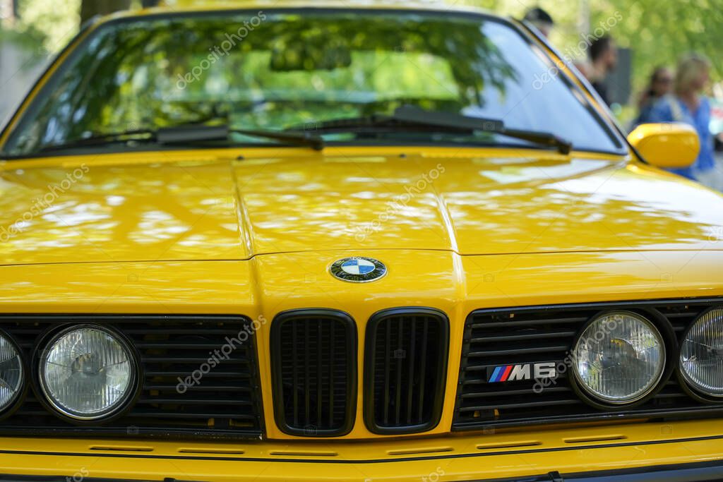 Germany Berlin May 11, 2025. Front view of a yellow BMW M6 with a black grille and classic M logo. The car reflects the light from the trees and appears both powerful and elegant.