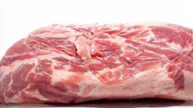 Beyaz arka planda büyük bir parça çiğ domuz yatıyor. Parlak, taze yüzey eşit dönüyor..