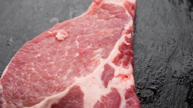 Tek, ince bir domuz pirzolası siyah bir taş levhanın üzerinde duruyor. Et dönüşümlü olarak, taneciklerini detaylıca ortaya koyar..