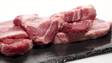 Bir yığın çiğ domuz pirzolası siyah bir taş levhanın üzerinde duruyor. Dönen et, keskin kenarları ve bilyeyi ortaya çıkarıyor..