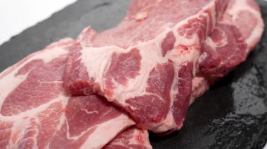 Koyu bir levhada çiğ domuz eti. Koyu bir taş levhanın üzerinde birkaç taze domuz pirzolası var. Sulu, mermer et yavaşça döner ve dokusunu ortaya çıkarır..