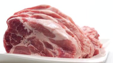 Beyaz tabakta çiğ et. Bir yığın çiğ domuz beyaz tabakta döner. Taze mermer, açık arkaplanda belirgin bir tezat oluşturur..