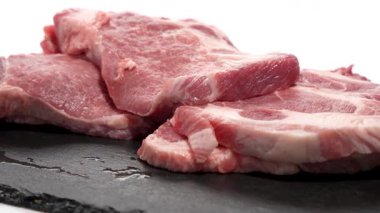 Koyu bir tabakta et dilimleri. Birkaç domuz pirzolası koyu bir taş levhanın üzerinde üst üste yatar. Et yavaşça döner ve mermer dokusunu ortaya çıkarır..