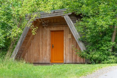 Turuncu kapılı küçük bir ahşap kulübe yoğun yeşilliklerle çevrili duruyor. İnşaat basit ve işlevsel..