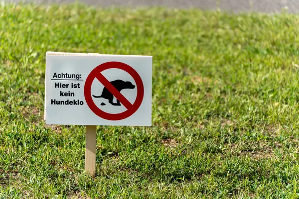 Çayır üzerindeki bir tabela uyarır: burada köpek tuvaleti yasaktır. İçki yasağı işareti kırmızı bir yasak sembolü olan bir köpeği gösteriyor.