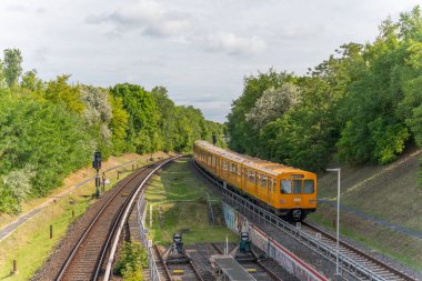 Almanya 7 Haziran 2025. Metro treni yeşil bir arazide raylar üzerinde hareket eder. Tren hafif bir viraja girer..