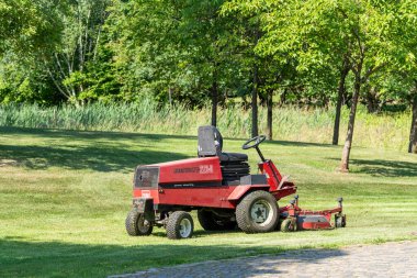 Germany Berlin June 18, 2025. A red riding lawnmower stands ready on a well-kept park lawn. The scene depicts tranquility and technical maintenance.