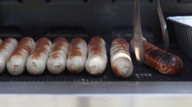 Sosisler döndü. Izgara ustası sosisleri dikkatlice maşayla çeviriyor. Mükemmel yemek pişirme noktası yaklaşıyor..