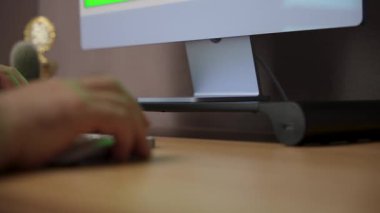 The camera glides past a computer stand holding a monitor with a vivid green screen. A hand reaches toward the keyboard in a smooth side-angle tracking shot.