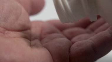 Kapsüller bir ele düşüyor. Beyaz kapsüller bir kutudan bir ele dökülür. Görüntü, ilaç ya da beslenme takviyesi alma anını iletir..