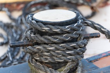 İskelede ahşap bir kordona sarılı sarılı halat örülmüş dokuyu ve deniz donanımını aydınlatıyor. Deniz atmosferiyle dolu bir demirleme sahnesi.