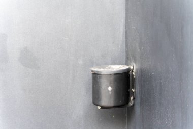 Duvara monte edilmiş siyah bir kül tablası gri bir duvara bağlıdır. Yakın plan halka açık sigara içme alanları için basit tasarımı gösteriyor.